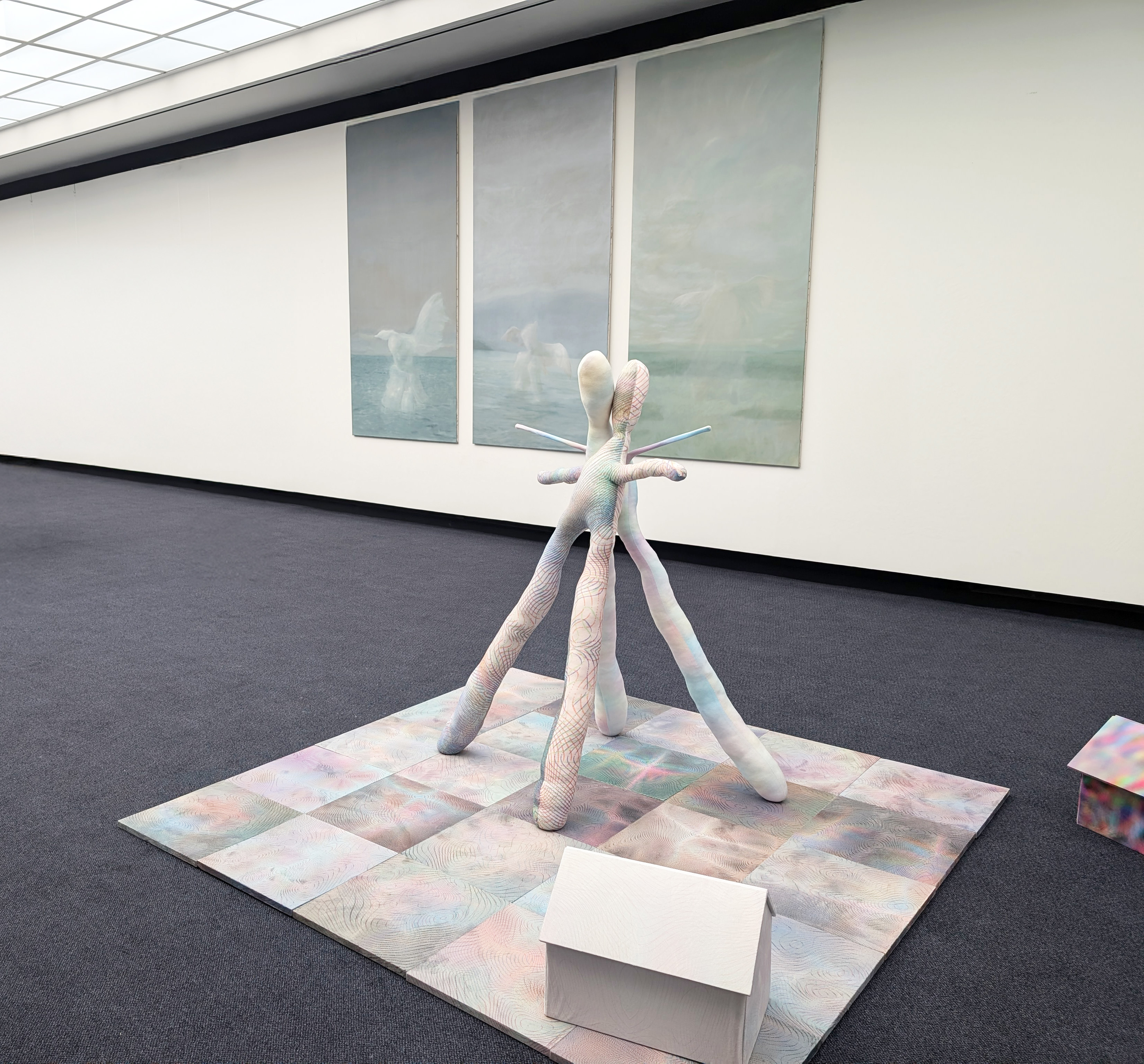 Tejzt’s Skulptur 'Variantenraum 934' – Eine weiche, humanoide Figur mit ausladenden Gliedmaßen erhebt sich aus einem irisierten, geometrisch strukturierten Boden. Die Textur erinnert an topografische Karten oder neuronale Netzwerke.