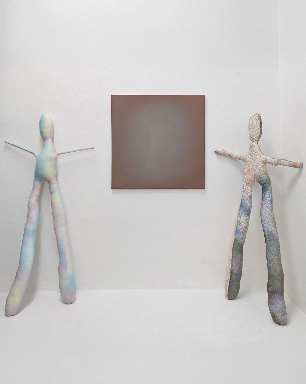 Tejzt — installation view: two elongated Hekling textile figures flanking a blurred square painting (2025)