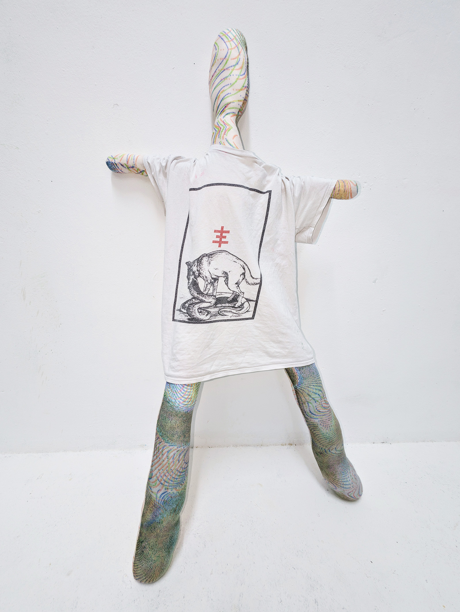 Tejzt — Hekling textile figure wearing printed T-shirt, wall-mounted installation view (2025)