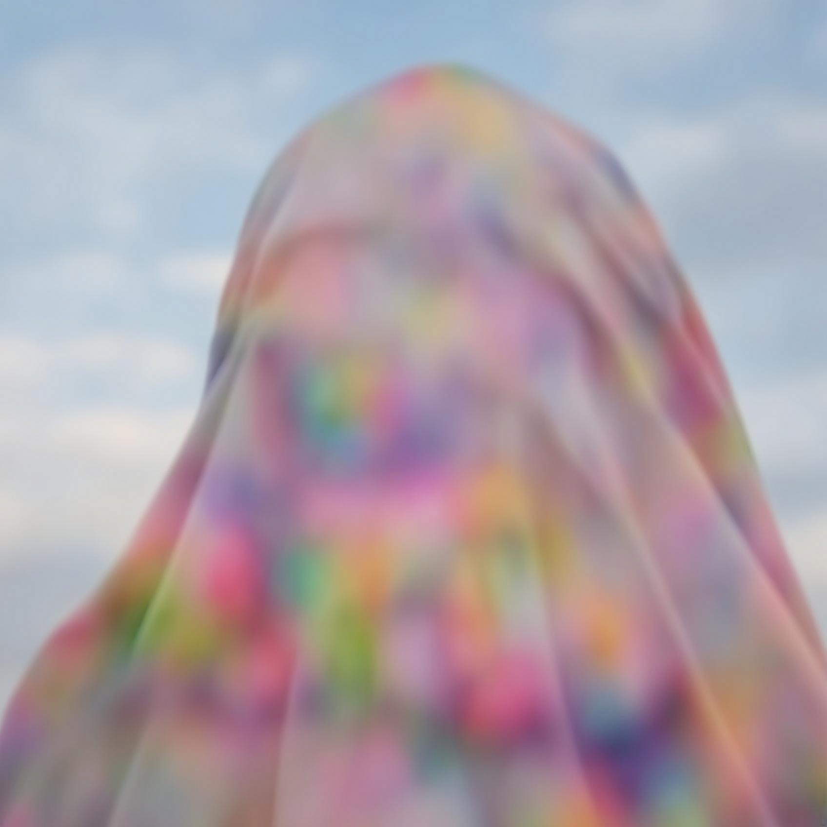 Tejzt – künstlerisches Porträt unter einem transparenten, irisierenden Schleier vor blauem Himmel